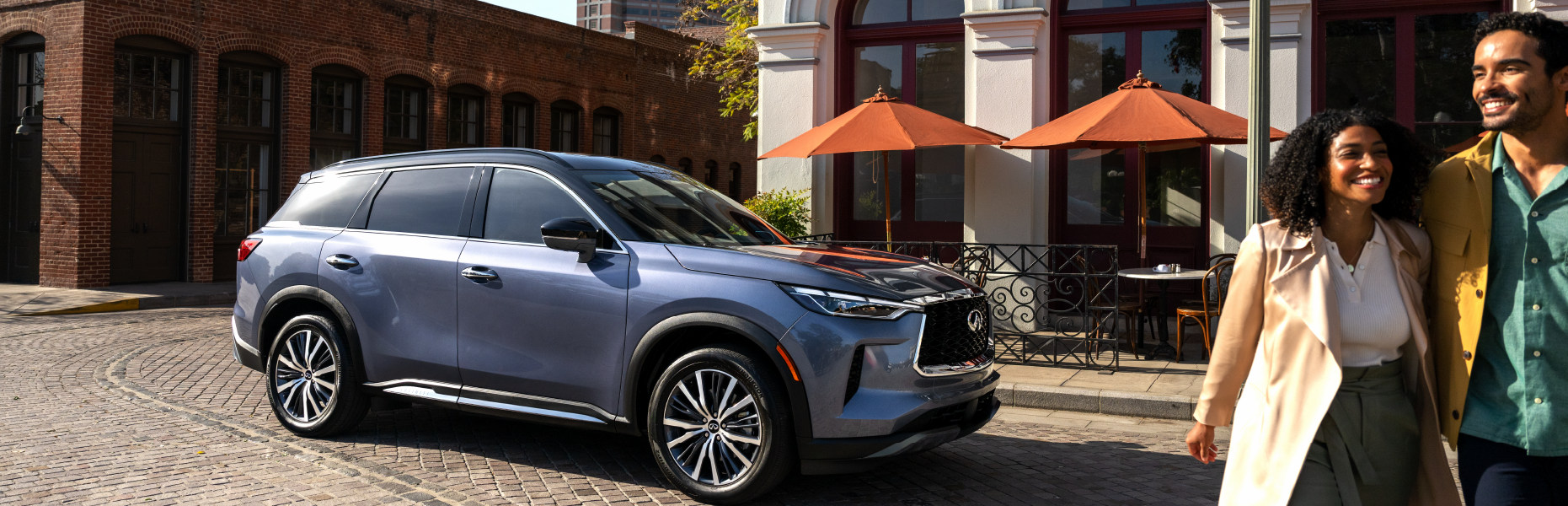 INFINITI QX60 parked on a cobblestone street beside a smiling couple walking by a restaurant